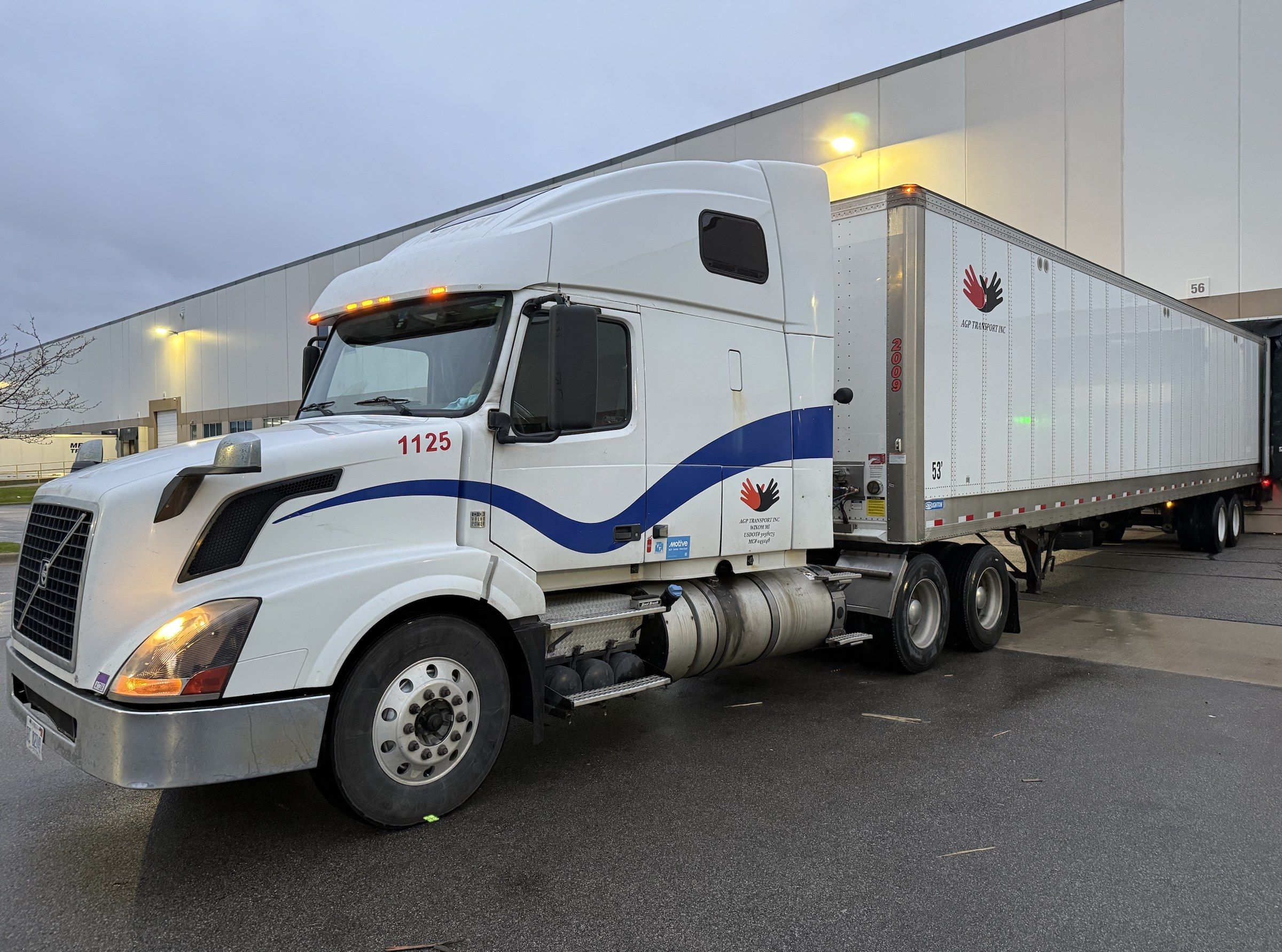 White and blue Volvo tractor, AGP unit 1125, backed into a warehouse dock